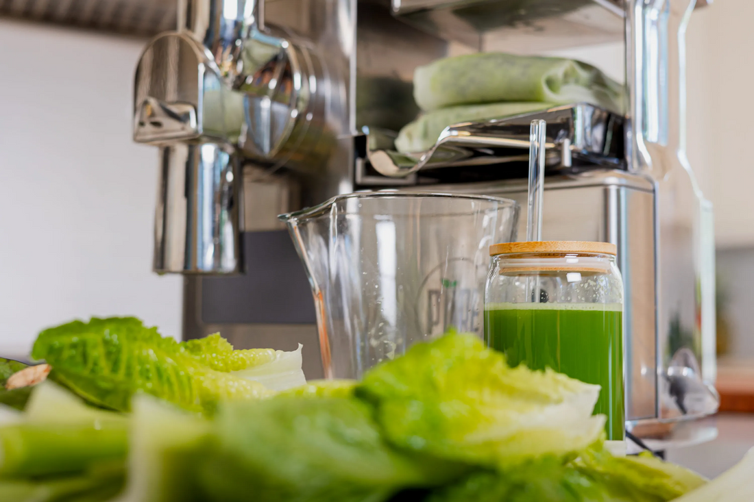 A jar of green celery juice in front of a PURE Juicer, with fresh greens