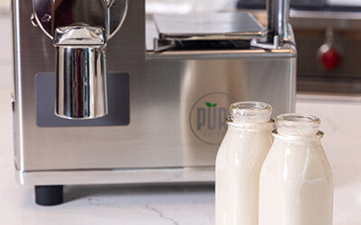 Two bottles of homemade almond milk in front of the PURE Juicer