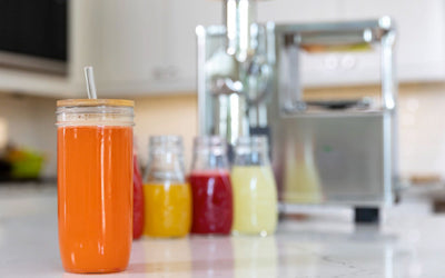 Jars of orange, yellow, red and pale green juice in front of a PURE Juicer