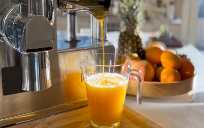A glass of citrus juice and bottles of juice next to the PURE Juicer