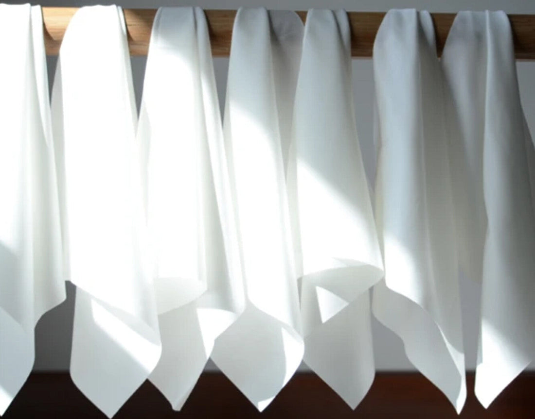 White press cloths hanging from a wooden rail in the sunlight