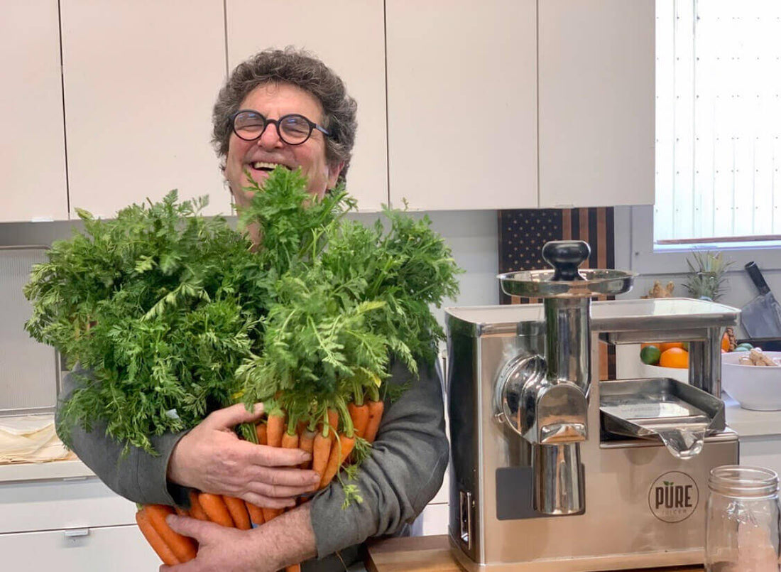 David Feinberg holding an armful of carrots next to the PURE Juicer