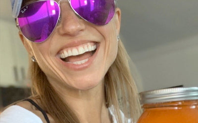 Erica Taft smiling in sunglasses, holding a jar of carrot juice