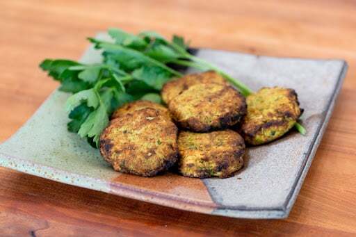 Four falafel patties on a ceramic plate with fresh parsley