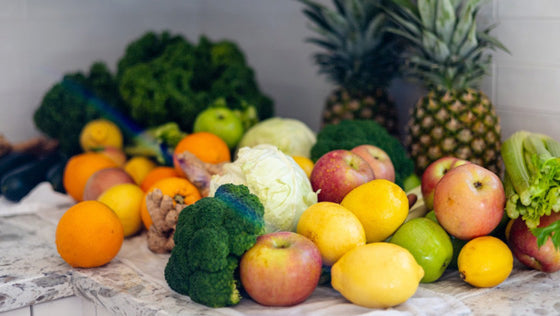 Pile of fresh oranges, lemons, apples, broccoli, kale and pineapples on a kitchen counter