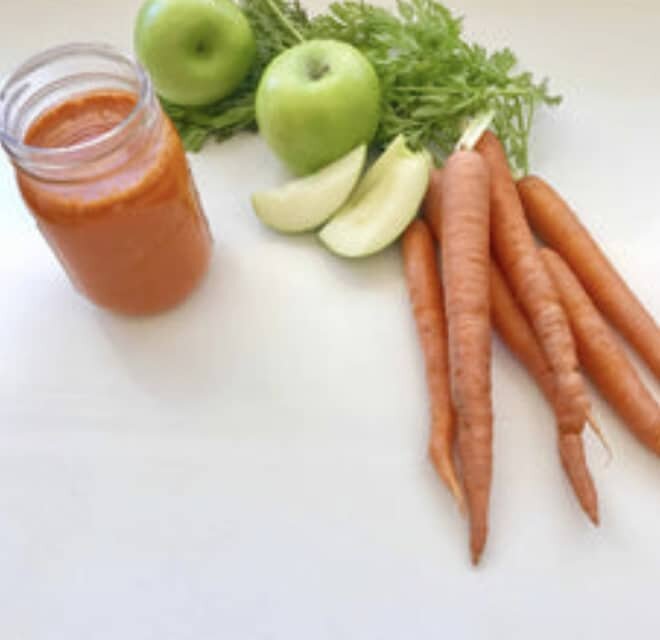 A jar of carrot-apple juice with carrots and green apples