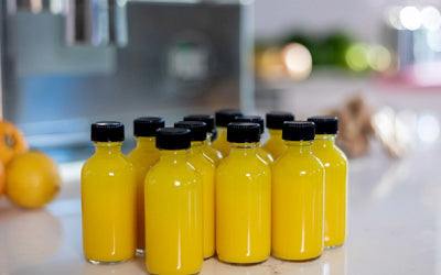 Small glass bottles of golden ginger turmeric orange lemon shots on a countertop