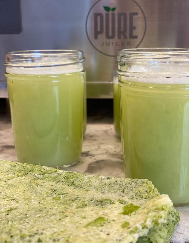 Two jars of fresh green juice beside a block of pressed vegetable pulp