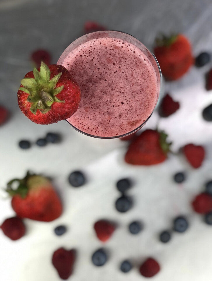 A strawberry smoothie in a glass among scattered strawberries and blueberries