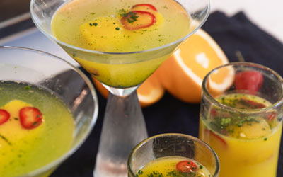 Orange-chili-matcha mocktails in martini glasses and tall glasses of juice on a black napkin