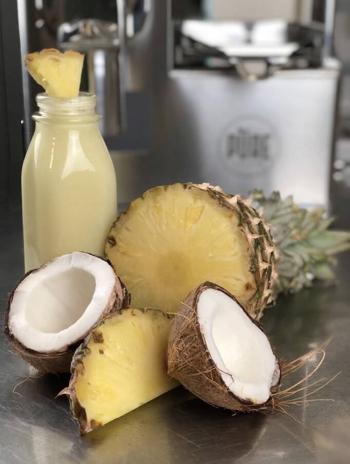 A bottle of pineapple-coconut juice beside a halved pineapple and coconut