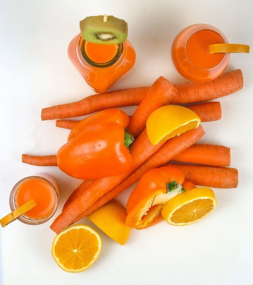 Carrots, orange bell peppers and oranges with glasses of orange juice