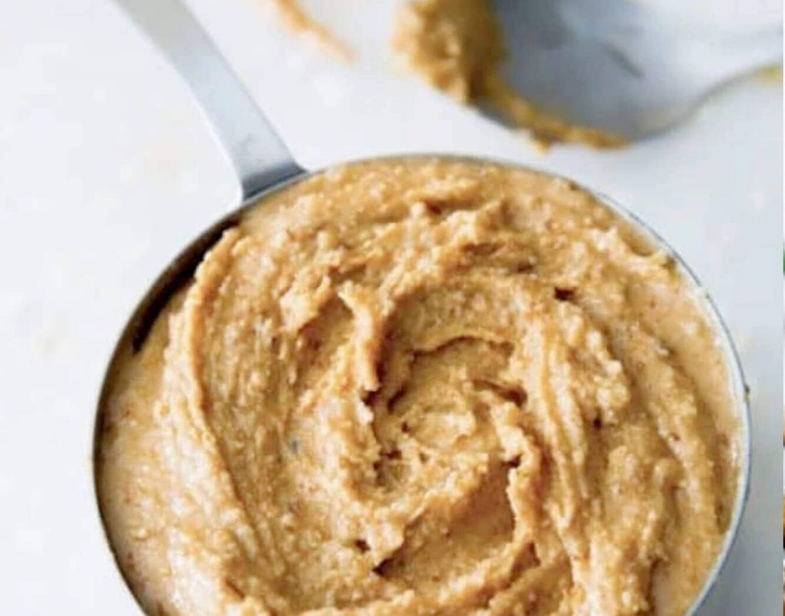 Homemade nut butter in a metal measuring cup with a spoon of nut butter beside it