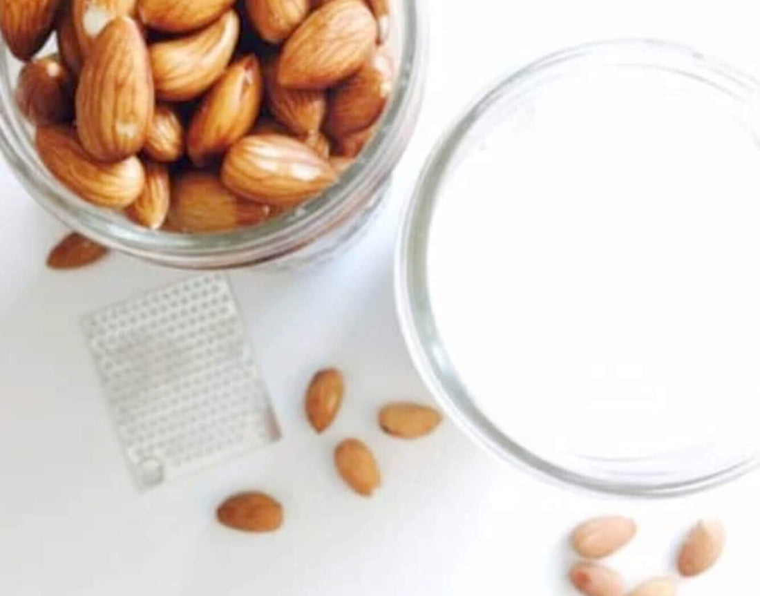 Raw almonds in a jar next to a glass of fresh almond milk
