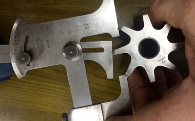 A hand holding a stainless steel cutter next to a measuring gauge