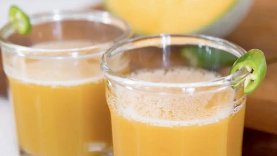 Two glasses of golden juice, each garnished with a slice of green pepper