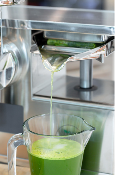 Green juice flowing from the PURE Juicer press into a glass pitcher