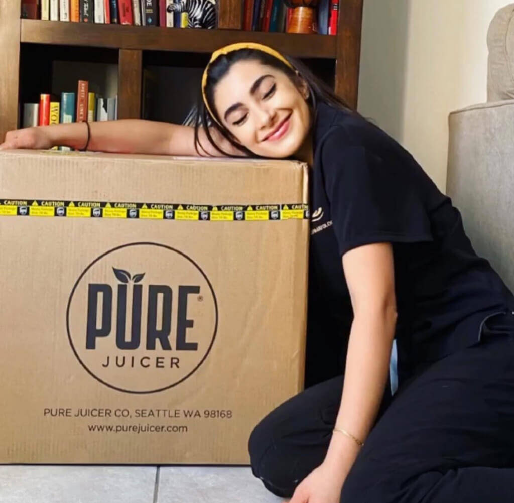 Ana Celia smiling and leaning on a PURE Juicer shipping box