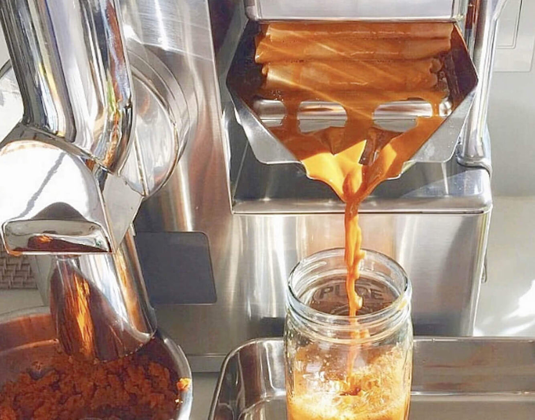 Orange juice pouring from the PURE Juicer press into a glass jar