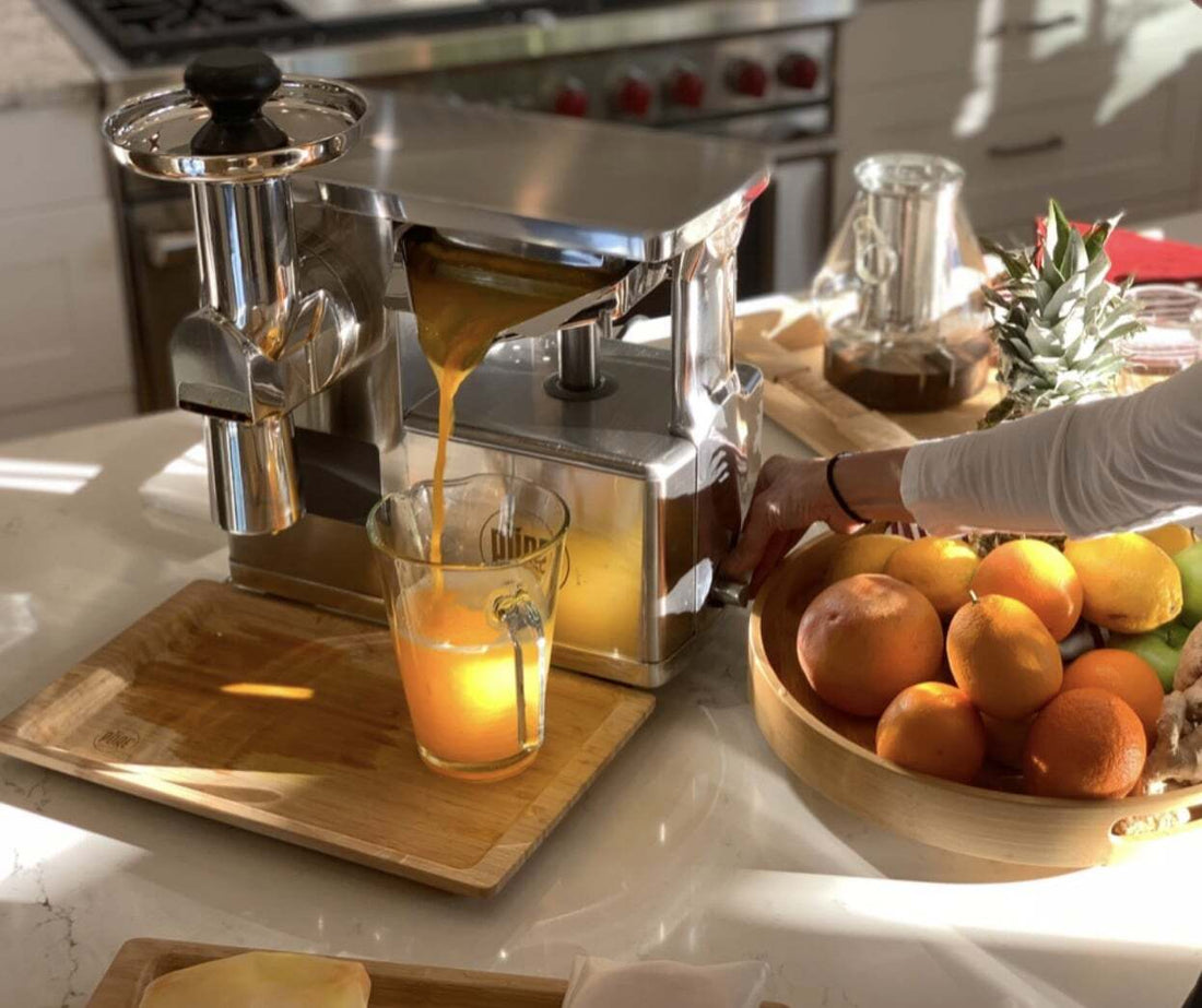 A PURE Juicer pressing golden juice into a glass beside a bowl of oranges