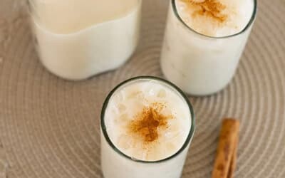 Two glasses of creamy tiger nut milk dusted with cinnamon, next to a bottle of tiger nut milk and a cinnamon stick