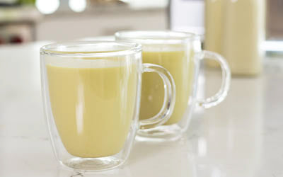Two glass mugs of turmeric milk on a kitchen counter